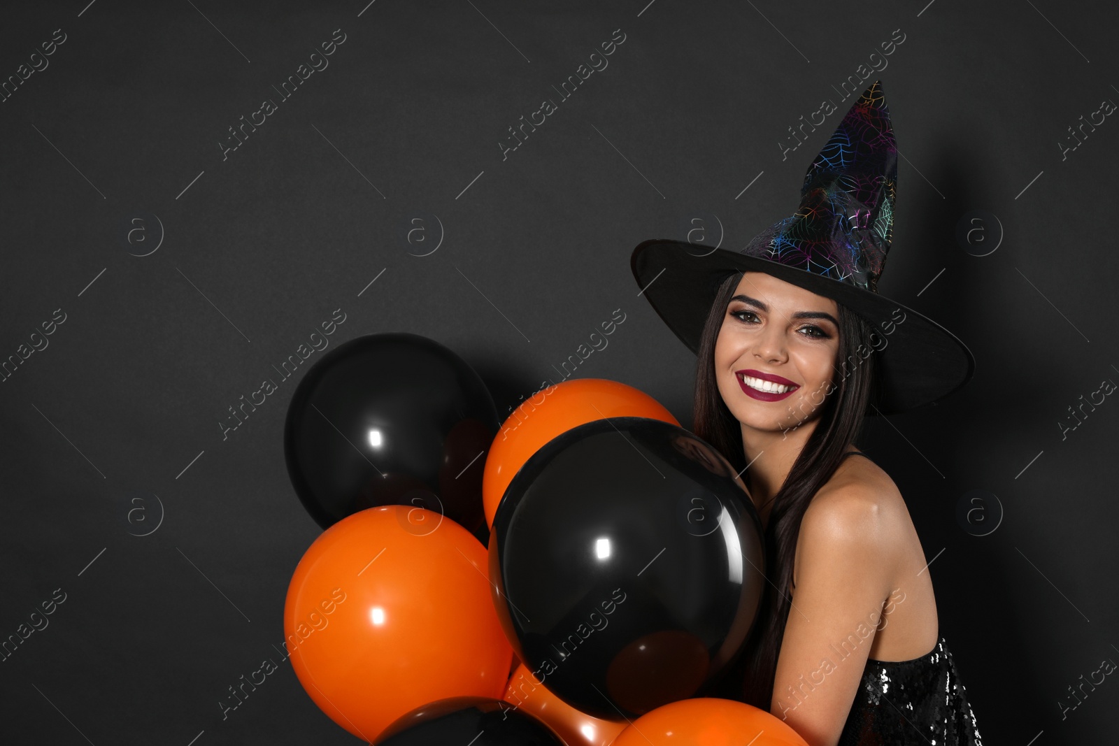 Photo of Beautiful woman wearing witch costume with balloons for Halloween party on black background