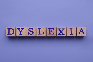 Wooden cubes with word Dyslexia on violet background, flat lay