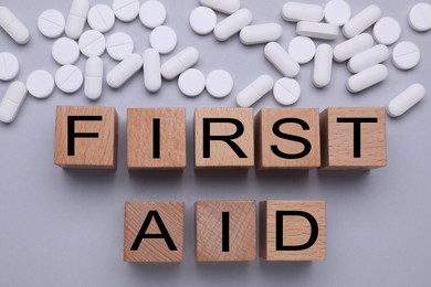Photo of Words First Aid made of wooden cubes and pills on grey background, flat lay