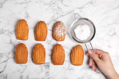 Woman decorating delicious madeleine cakes with powdered sugar at white marble table, top view