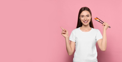 Photo of Beautiful young woman holding sushi with chopsticks on pink background. Space for text