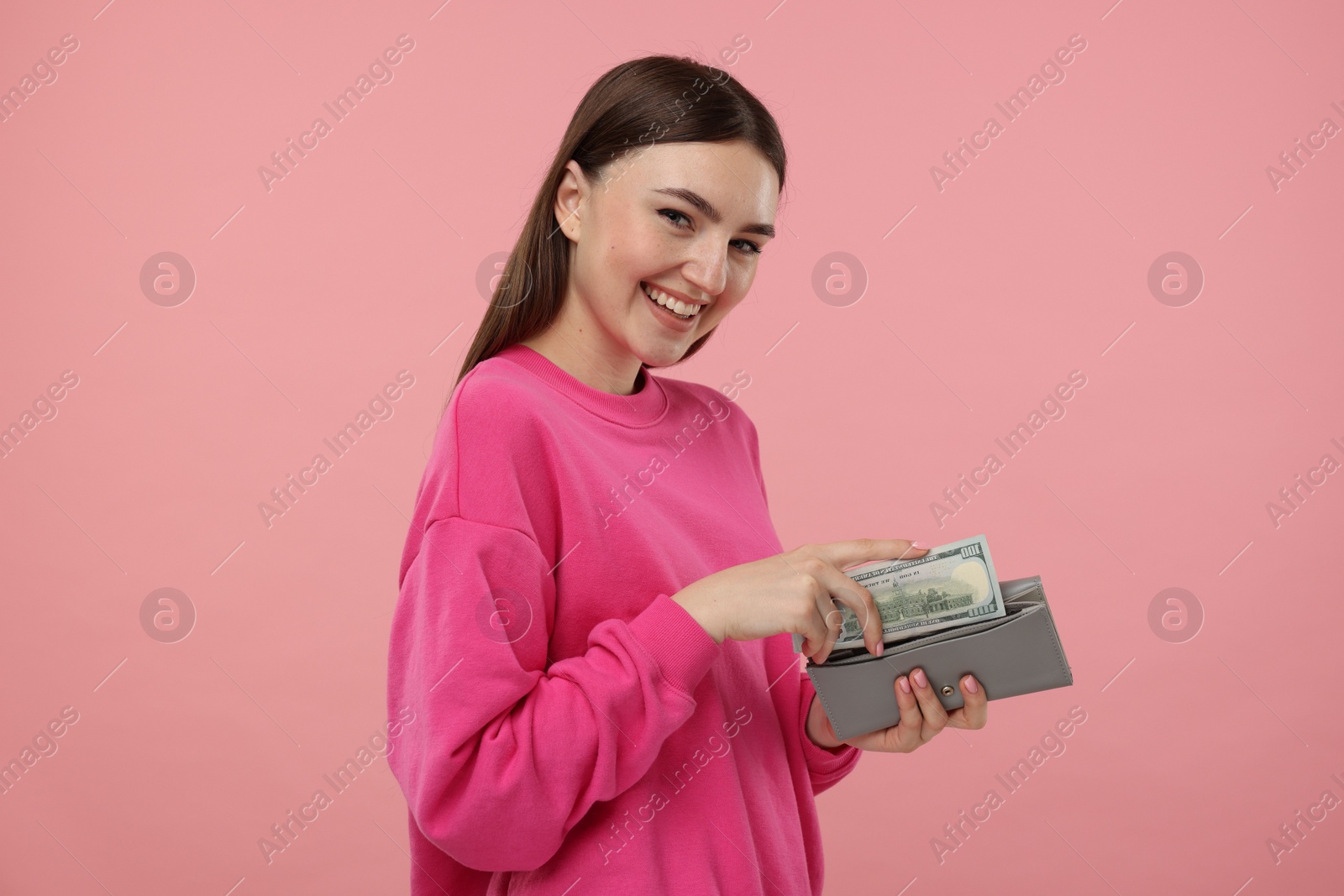 Photo of Happy woman putting money into wallet on pink background