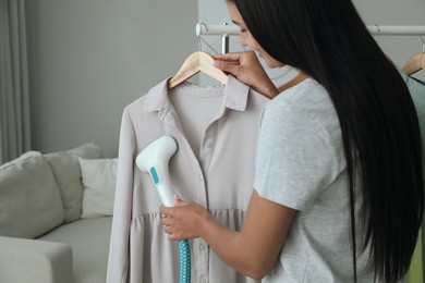 Photo of Woman steaming blouse on hanger at home, closeup