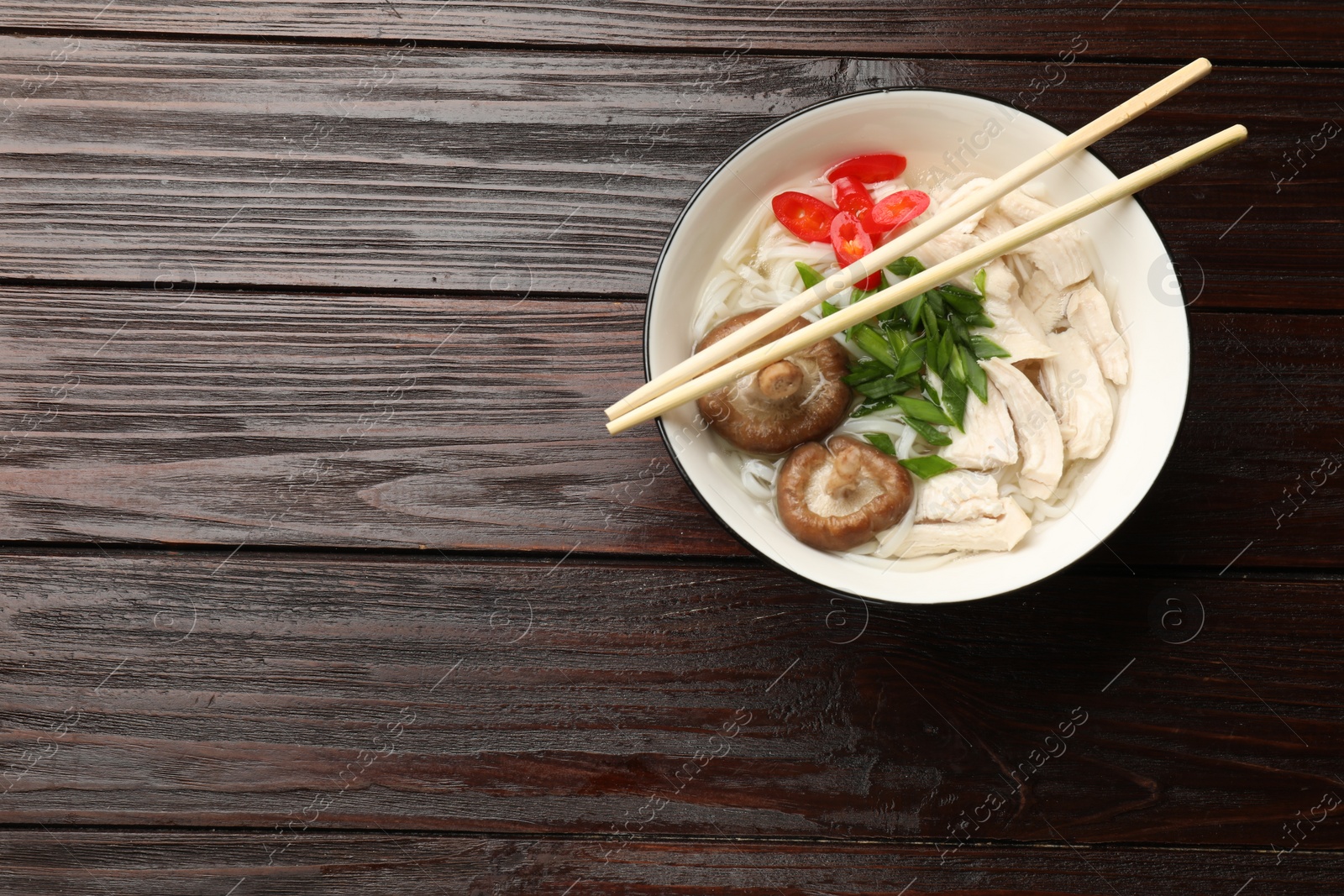 Photo of Delicious ramen with meat in bowl and chopsticks on wooden table, top view. Space for text