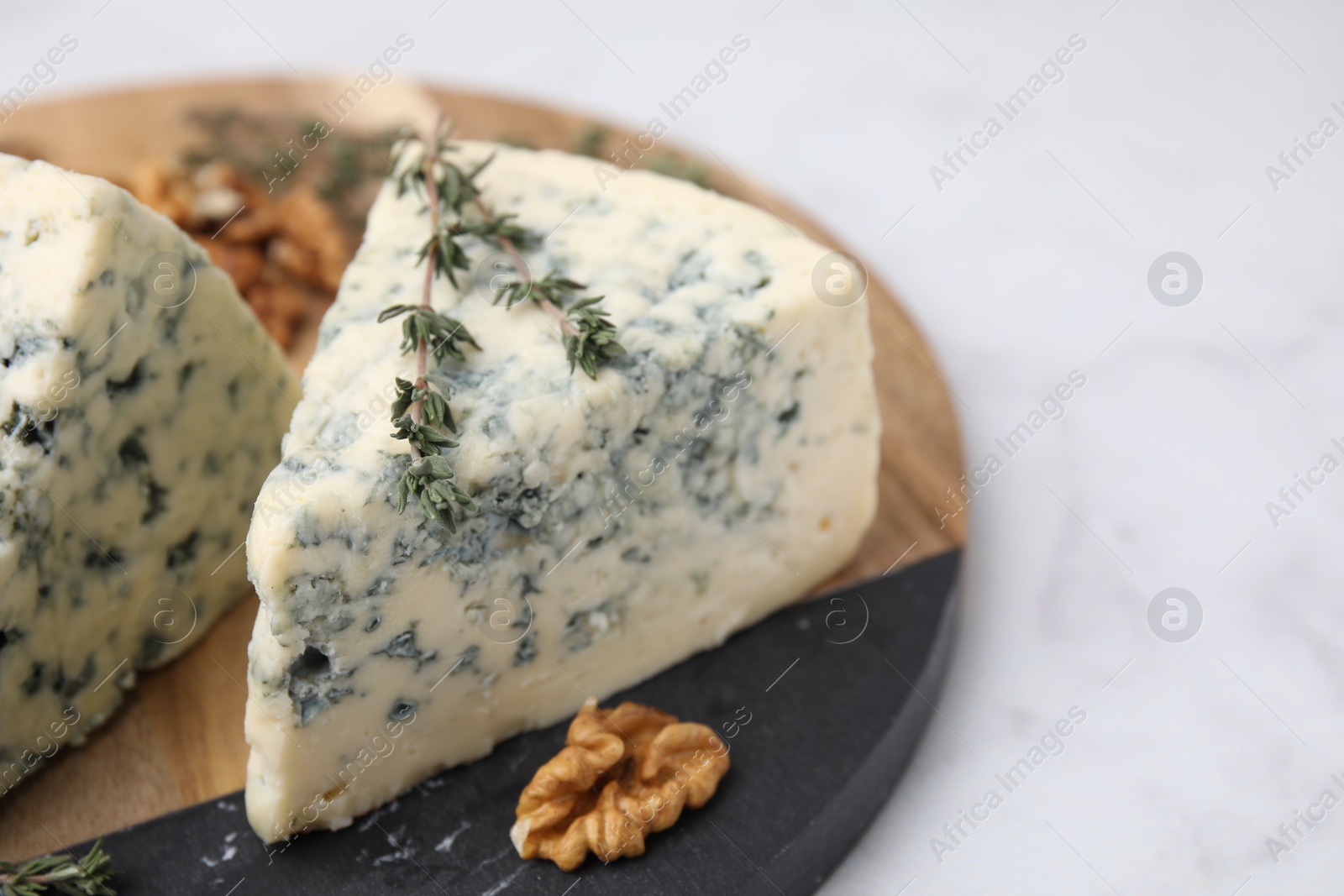 Photo of Tasty blue cheese with thyme and walnuts on white marble table, closeup. Space for text