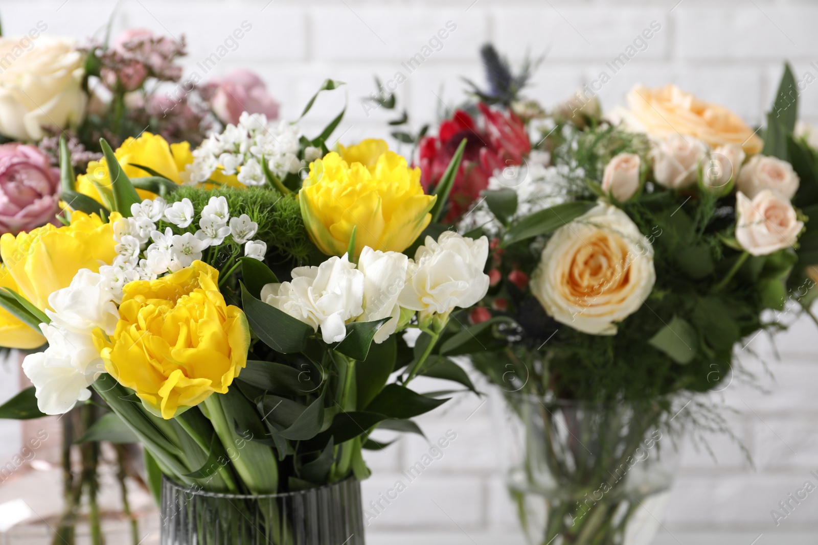 Photo of Beautiful bouquets with fresh flowers against white brick wall, closeup