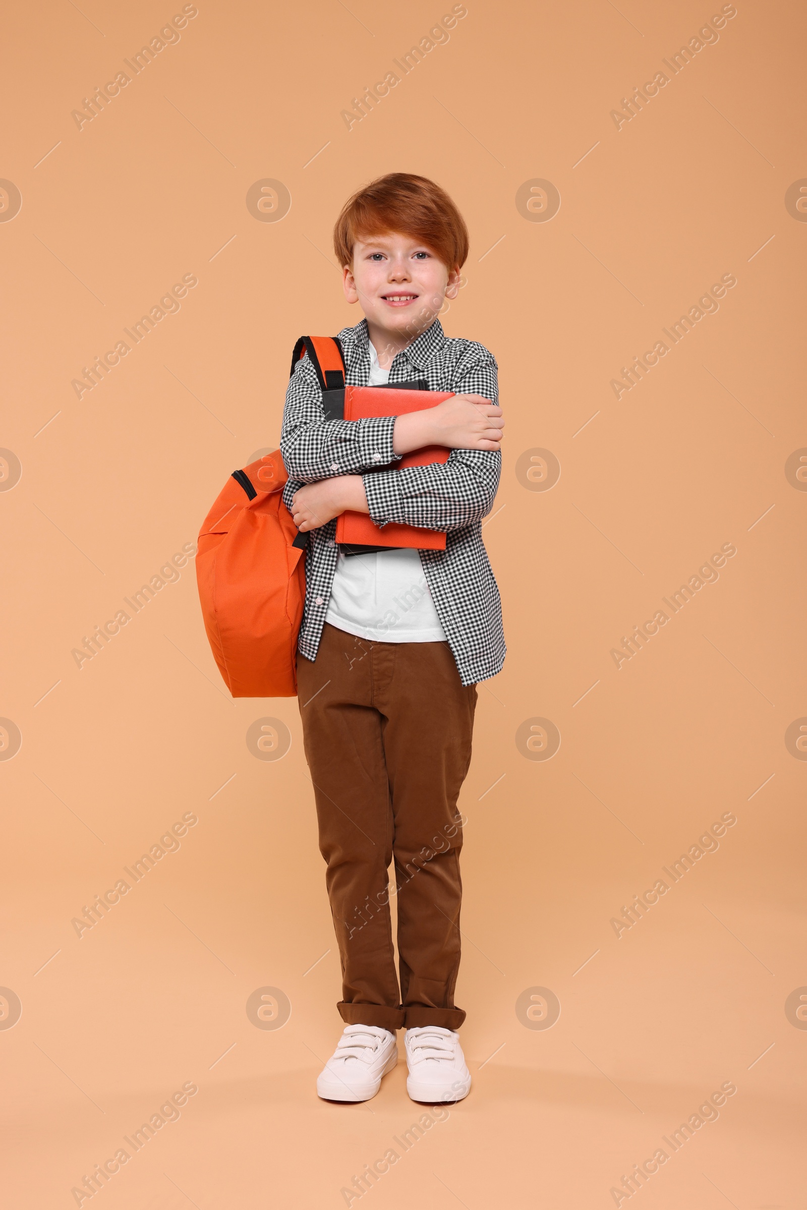 Photo of Smiling schoolboy with backpack and books on beige background