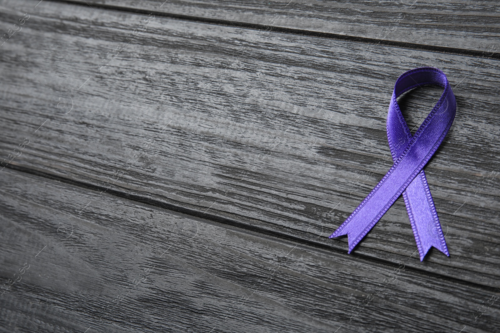 Photo of Purple ribbon on grey wooden background, space for text. Domestic violence awareness