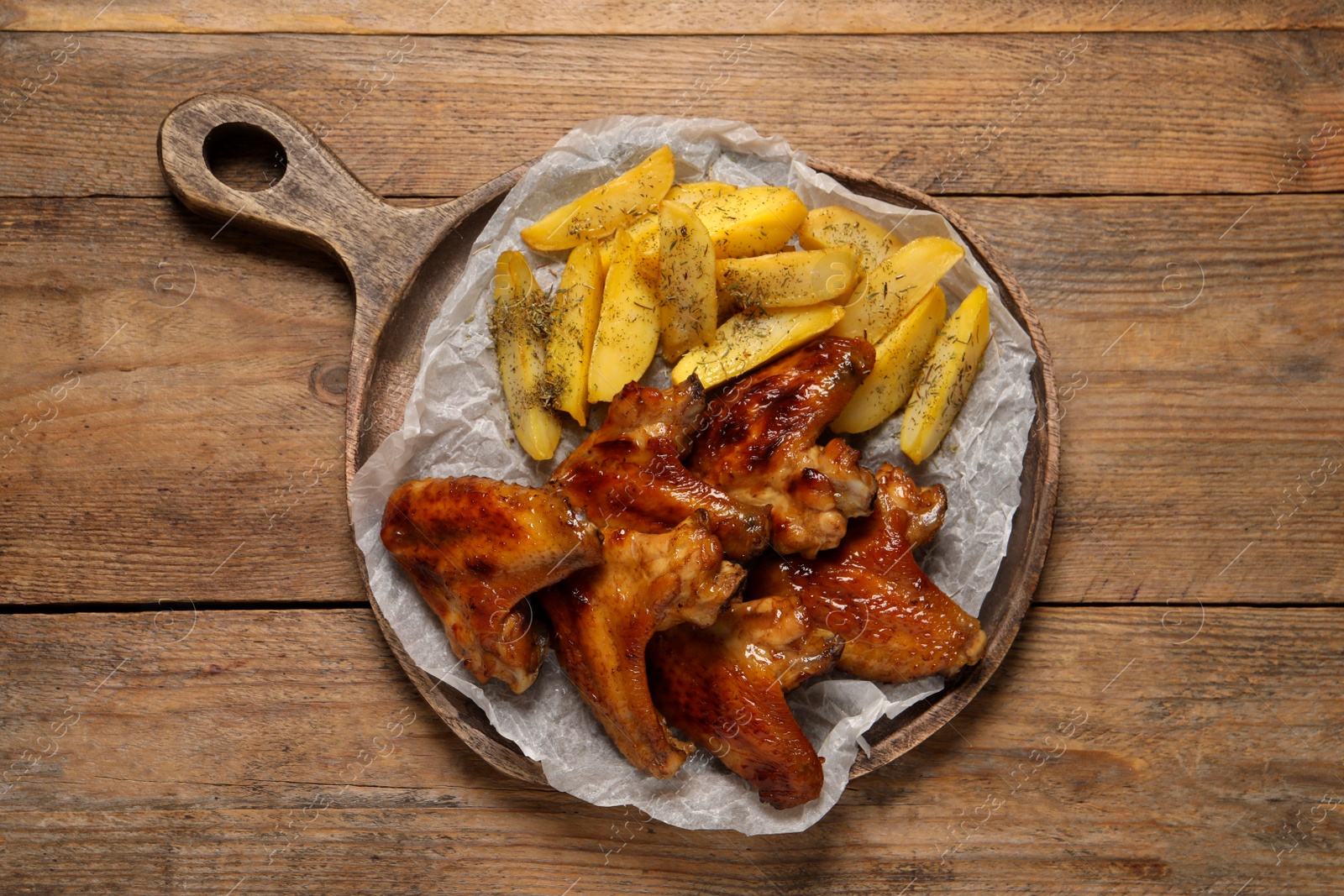 Photo of Board with delicious fried chicken wings and potatoes on wooden table, top view