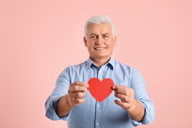 Photo of Happy mature man holding red paper heart on color background