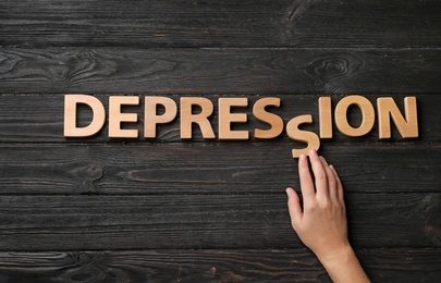 Photo of Woman making word Depression with letters on dark wooden background, top view