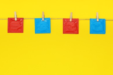 Clothesline with packaged condoms on yellow background, space for text. Safe sex