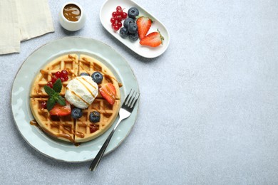 Delicious Belgian waffles with ice cream, berries and caramel sauce served on grey table, flat lay. Space for text