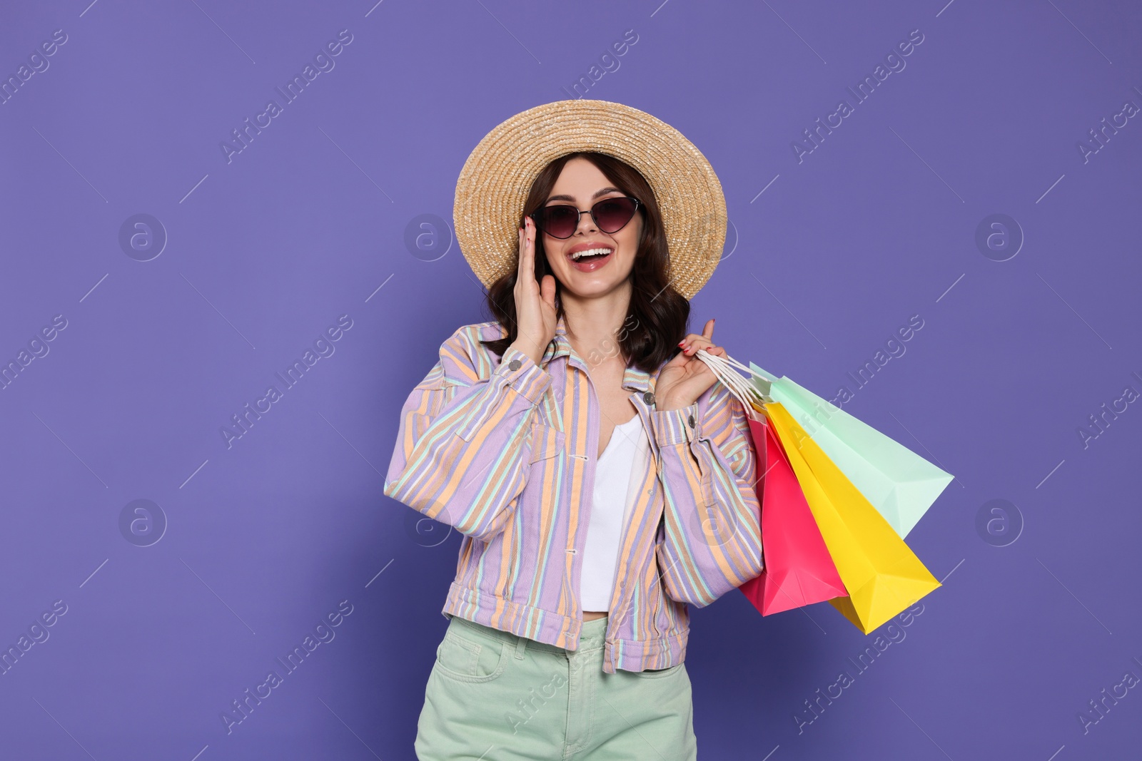 Photo of Beautiful young woman with paper shopping bags on purple background