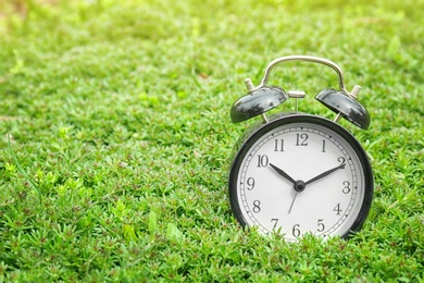 Photo of Alarm clock on green plants, outdoors. Time change concept