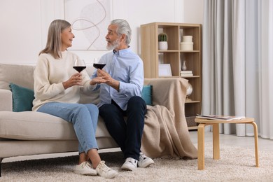 Affectionate senior couple with glasses of wine on sofa indoors