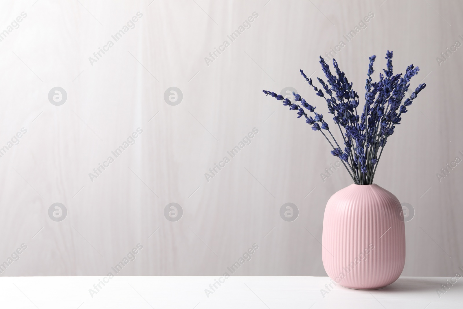 Photo of Bouquet of beautiful preserved lavender flowers on white table near grey wooden wall, space for text