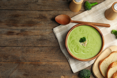 Photo of Delicious broccoli cream soup served on wooden table, flat lay. Space for text