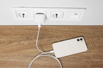 Modern smartphone charging on wooden table, above view