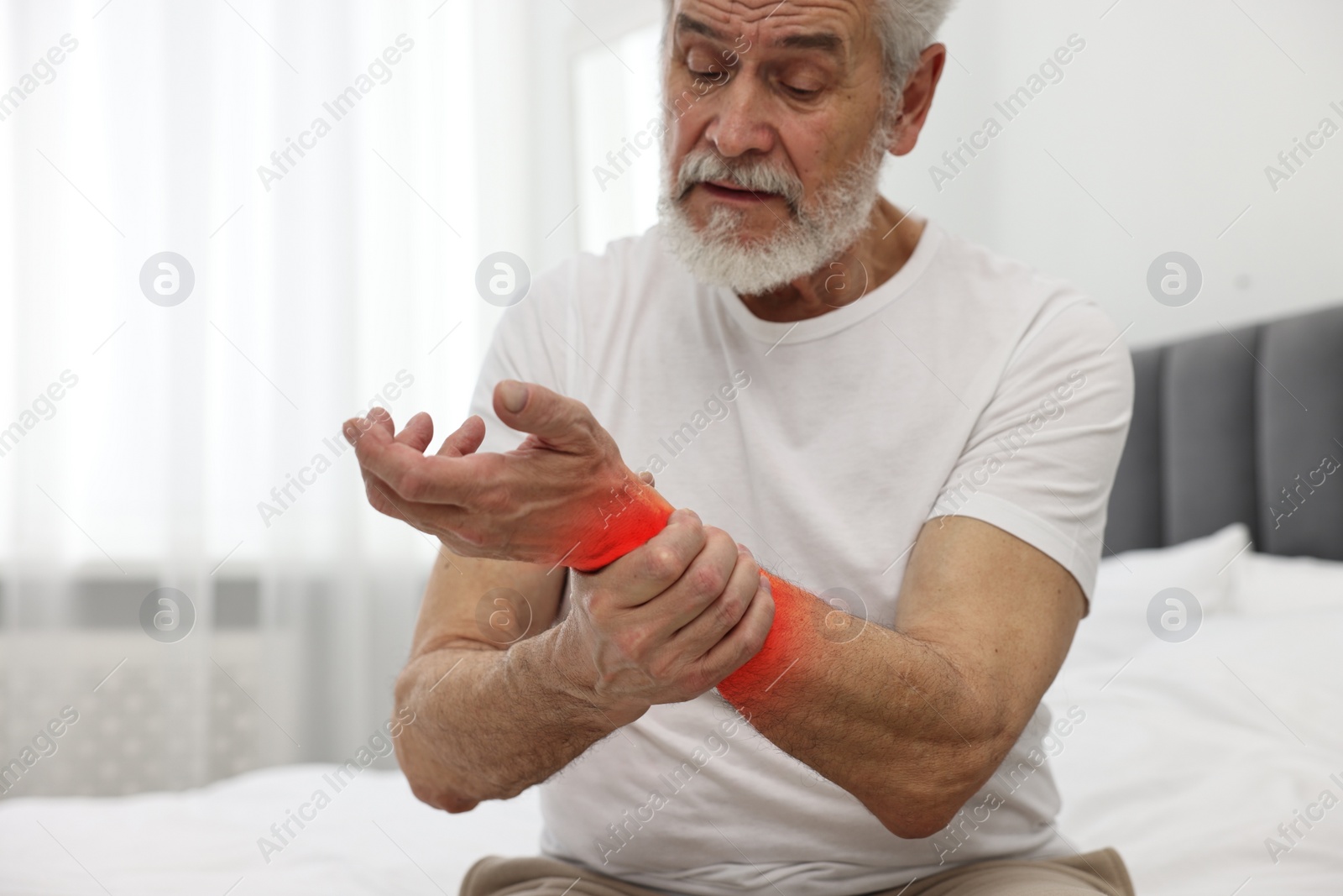 Image of Arthritis symptoms. Man suffering from pain in his wrist on bed indoors