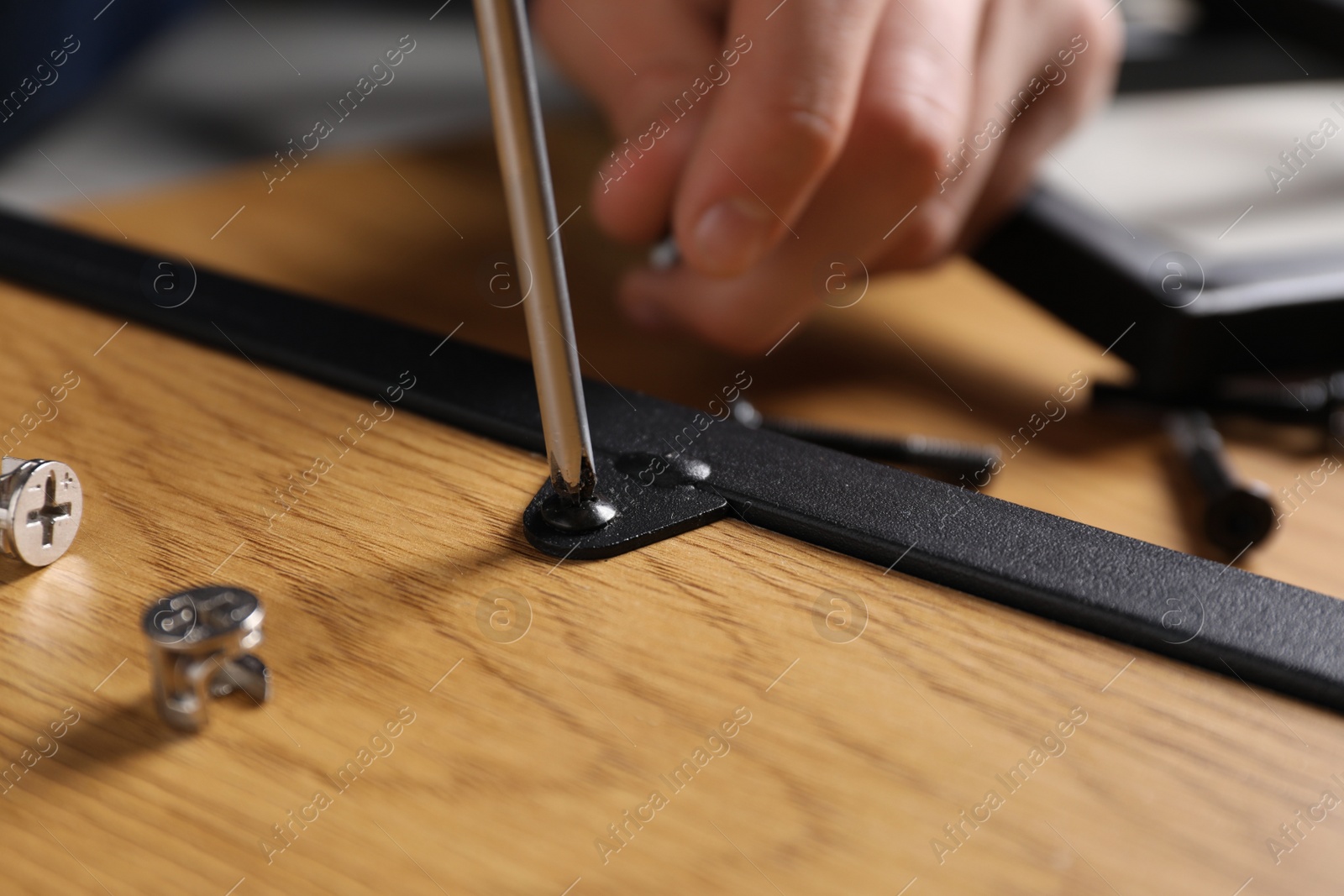 Photo of Man with screwdriver assembling wooden furniture indoors, closeup