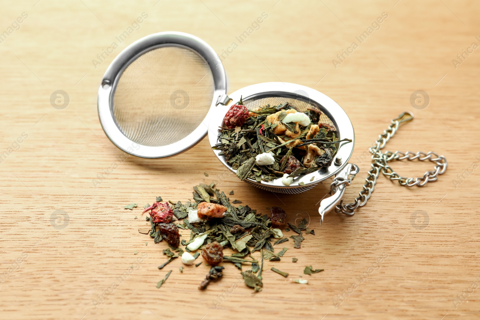 Photo of Snap infuser with dried herbal tea leaves on wooden table, closeup