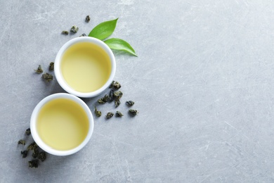 Photo of Cups of Tie Guan Yin oolong and tea leaves on grey background, top view with space for text