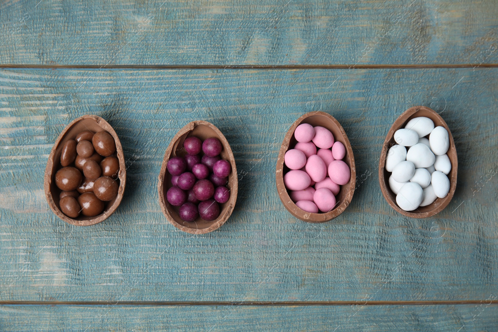 Photo of Broken chocolate Easter eggs with colorful candies on blue wooden table, flat lay