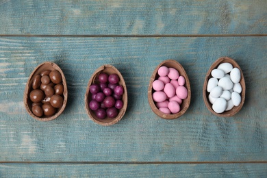 Broken chocolate Easter eggs with colorful candies on blue wooden table, flat lay