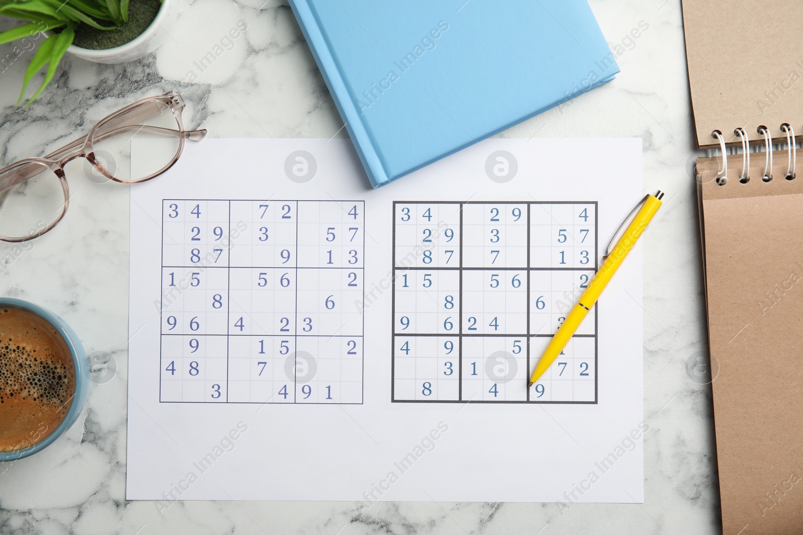 Photo of Sudoku, pen, planner, glasses and cup of coffee on white marble table, flat lay