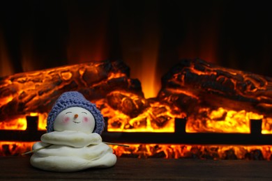 Cute decorative snowman in hat on wooden floor near fireplace, space for text