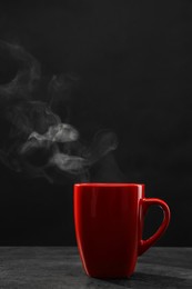 Steaming ceramic cup on grey table against dark background
