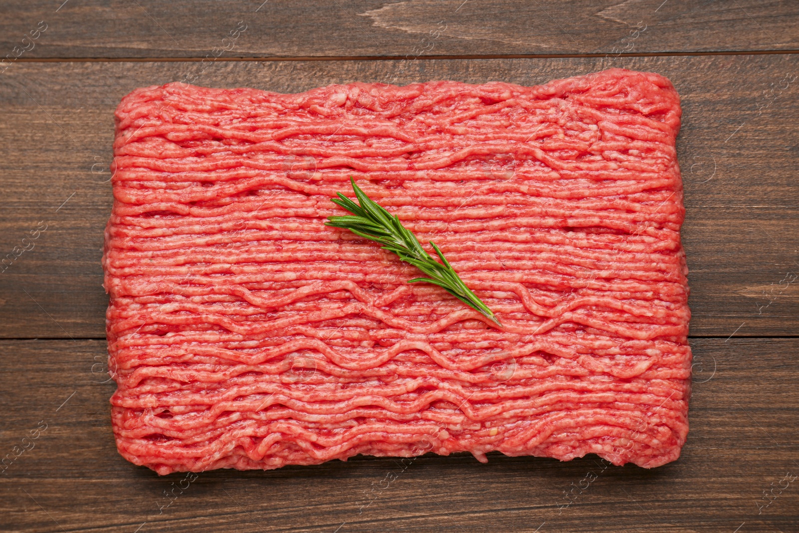 Photo of Raw fresh minced meat with rosemary on wooden table, top view