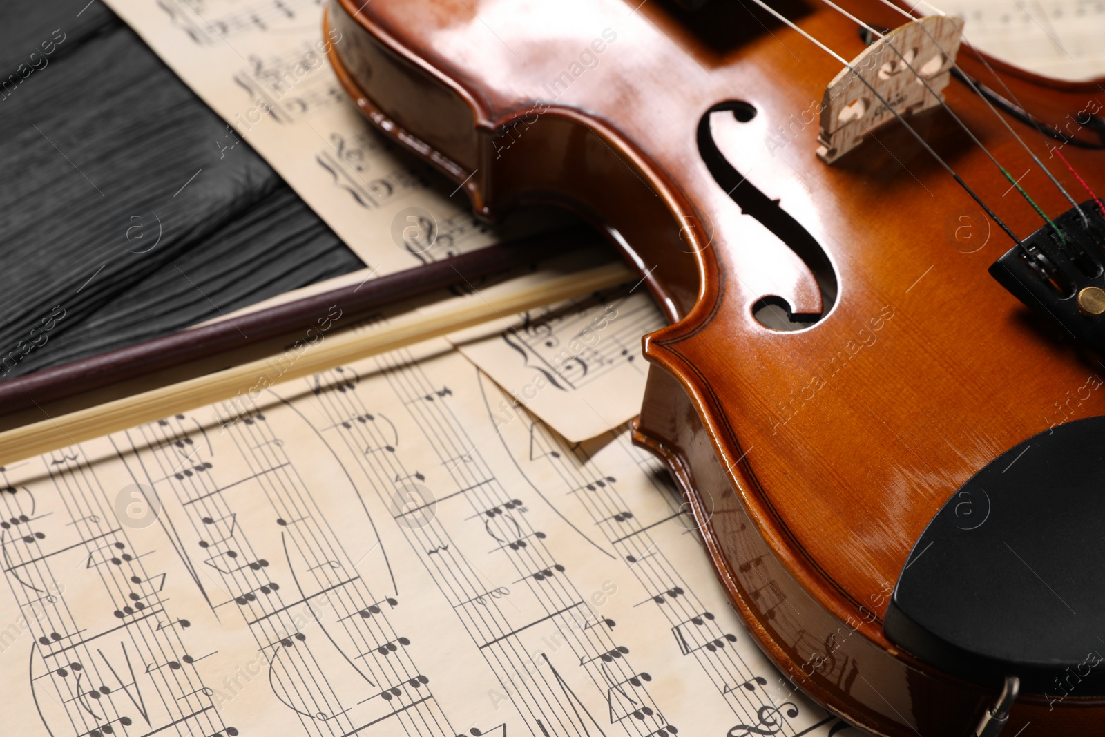 Photo of Violin, bow and music sheets on black wooden table, closeup