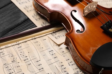 Photo of Violin, bow and music sheets on black wooden table, closeup