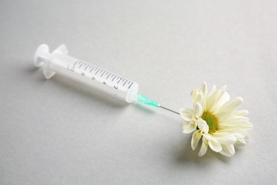 Photo of Medical syringe and beautiful chrysanthemum flower on grey background, closeup