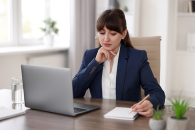 Woman taking notes during webinar at wooden table indoors