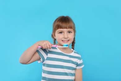 Little girl brushing teeth on color background