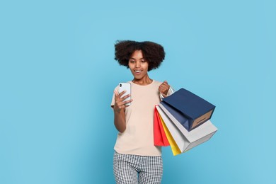 Photo of Happy African American woman with shopping bags and smartphone on light blue background