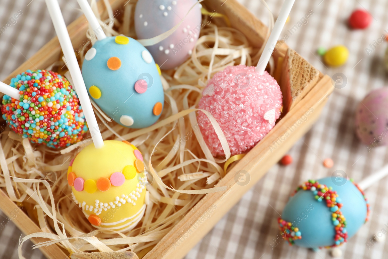 Photo of Delicious sweet cake pops in wooden crate on table, closeup. Easter holiday