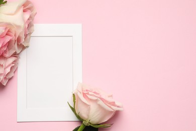 Empty white frame and beautiful roses on pink background, top view. Space for text