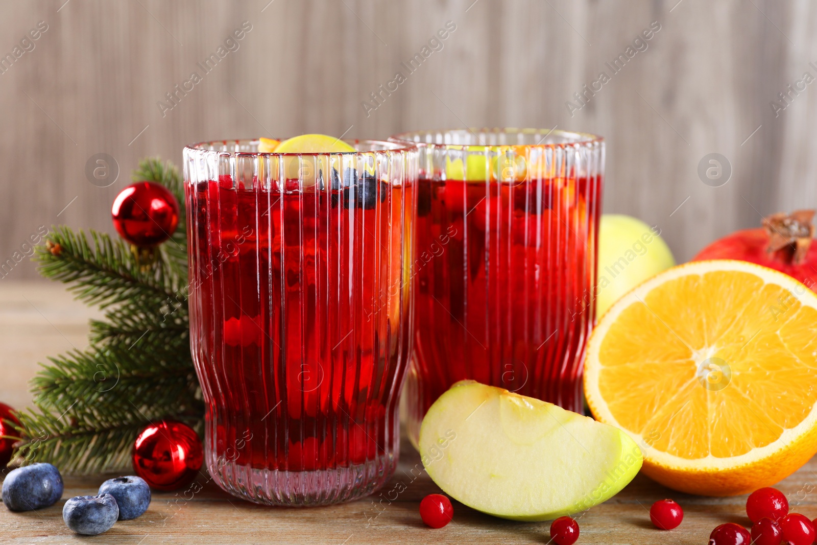 Photo of Aromatic Sangria drink in glasses, ingredients and Christmas decor on wooden table