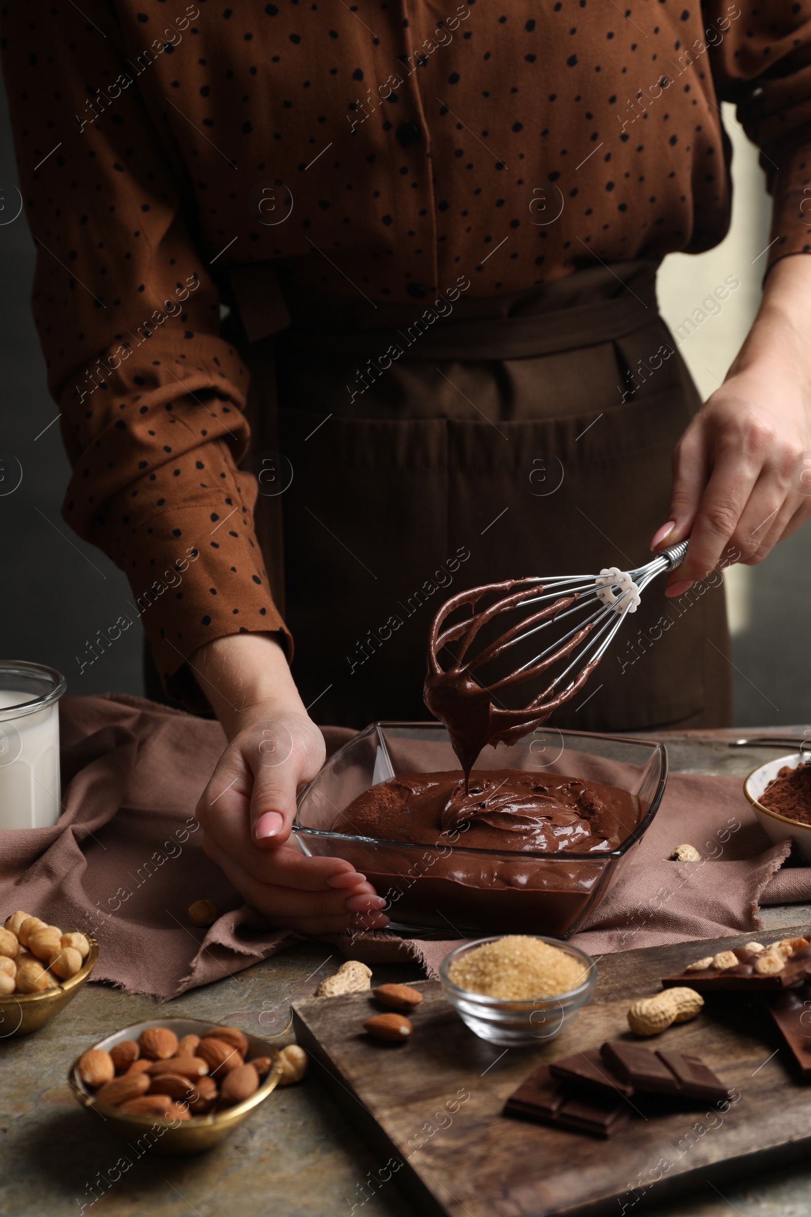 Photo of Woman mixing delicious chocolate cream with whisk at table, closeup