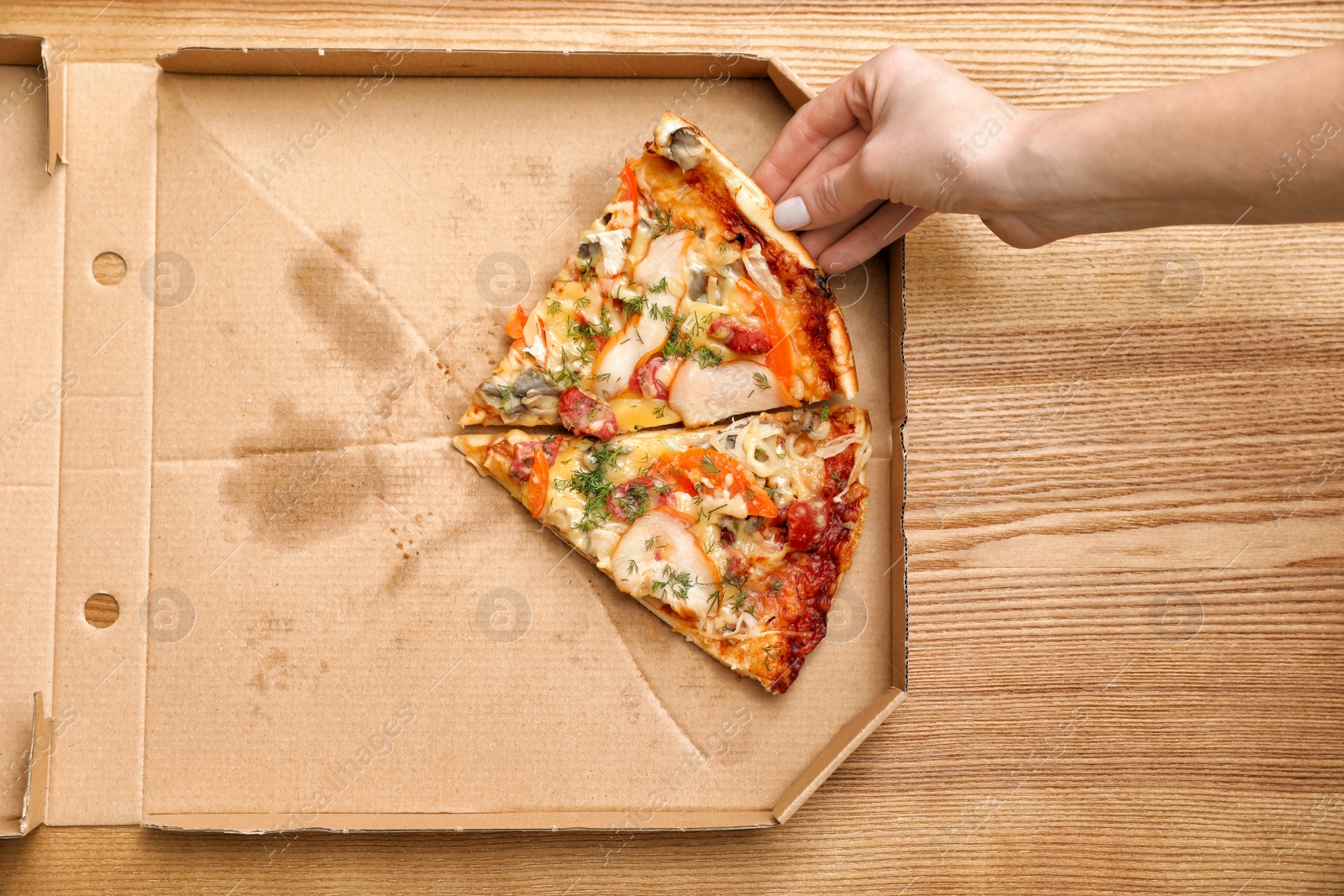 Photo of Woman taking pizza piece out of box on wooden table, top view