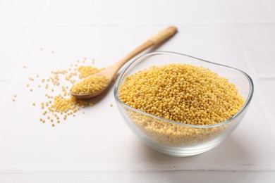 Millet groats in bowl and spoon on white tiled table