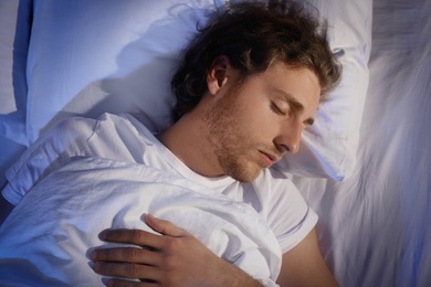 Photo of Handsome young man sleeping on pillow at night, top view. Bedtime