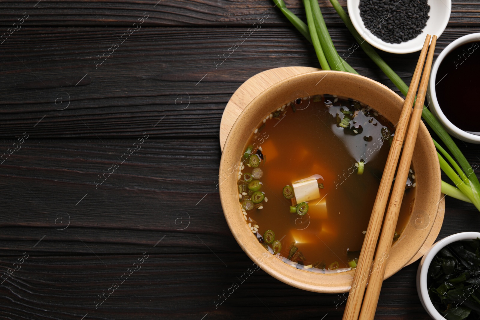 Photo of Bowl of delicious miso soup with tofu served on dark wooden table, flat lay. Space for text