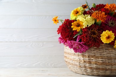 Beautiful wild flowers in wicker basket on light wooden table. Space for text