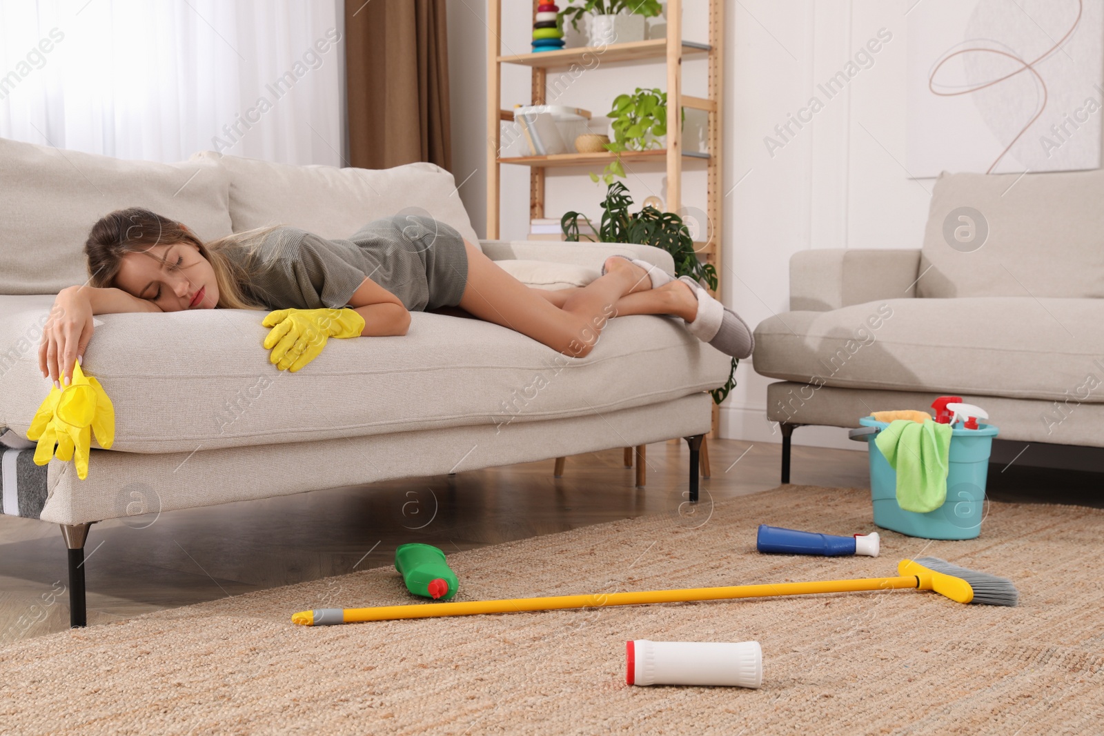 Photo of Tired young mother sleeping on sofa in messy living room