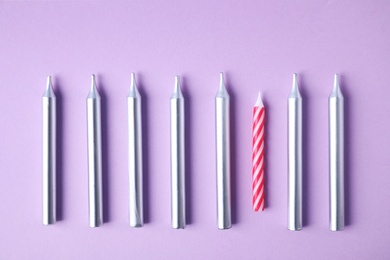 Bright birthday candles on lilac background, flat lay